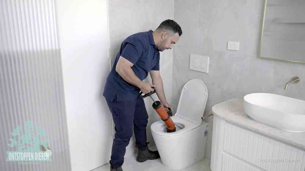 Een monteur buigt over een wandcloset en duwt met de hand een persluchtontstopper in de toiletpot om de verstopping handmatig los te maken in Dieren
