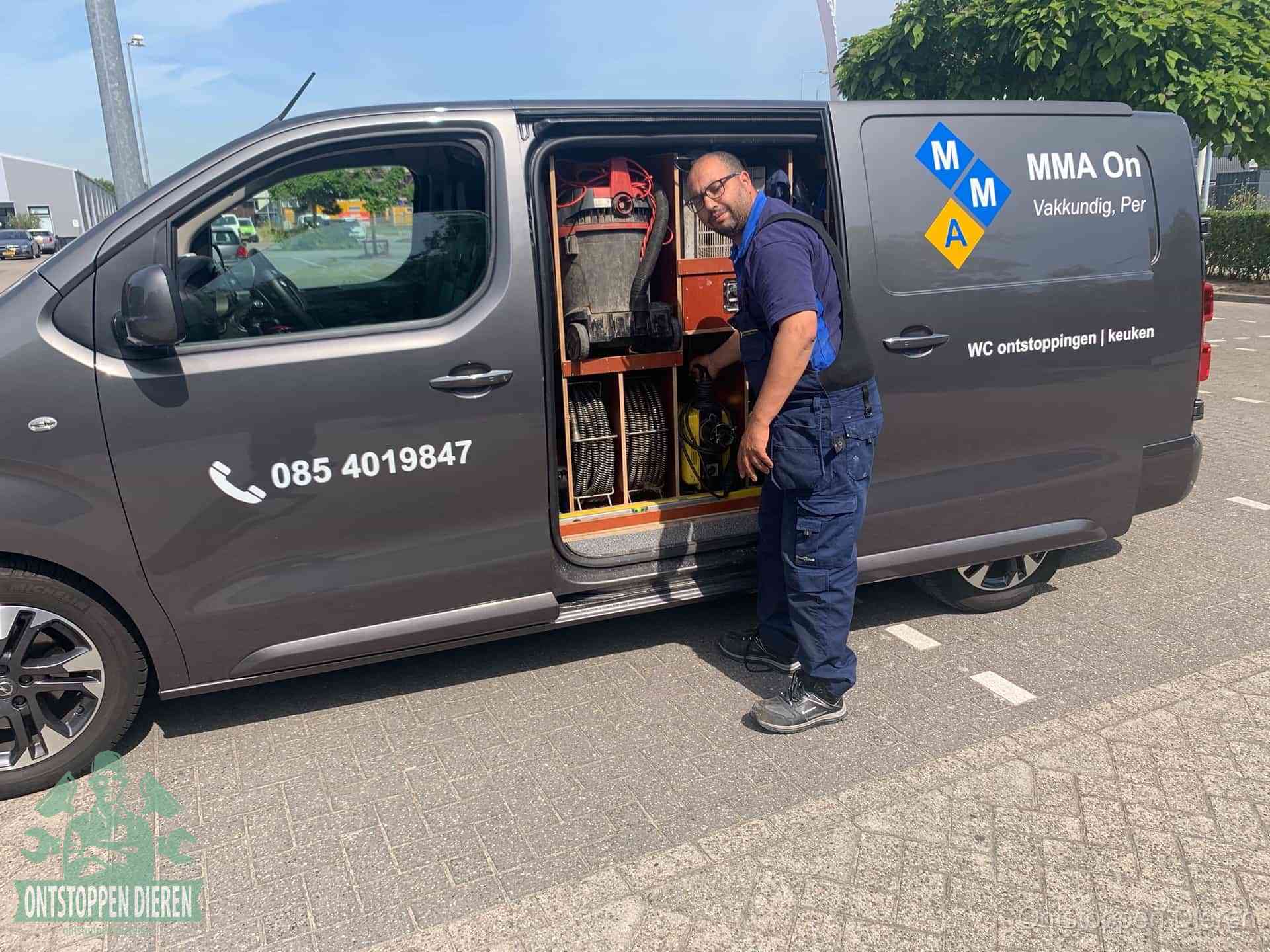 Een monteur bij de open schuifdeur van zijn bedrijfsbus op een parkeerplaats, klaar om de oorzaak van terugkerende afvoerverstoppingen aan te pakken in Dieren