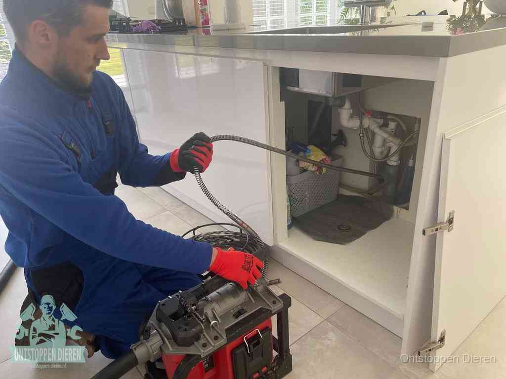 Een monteur reinigt de keukenafvoer grondig met een veermachine om terugkerende gootsteenverstoppingen te voorkomen in Dieren