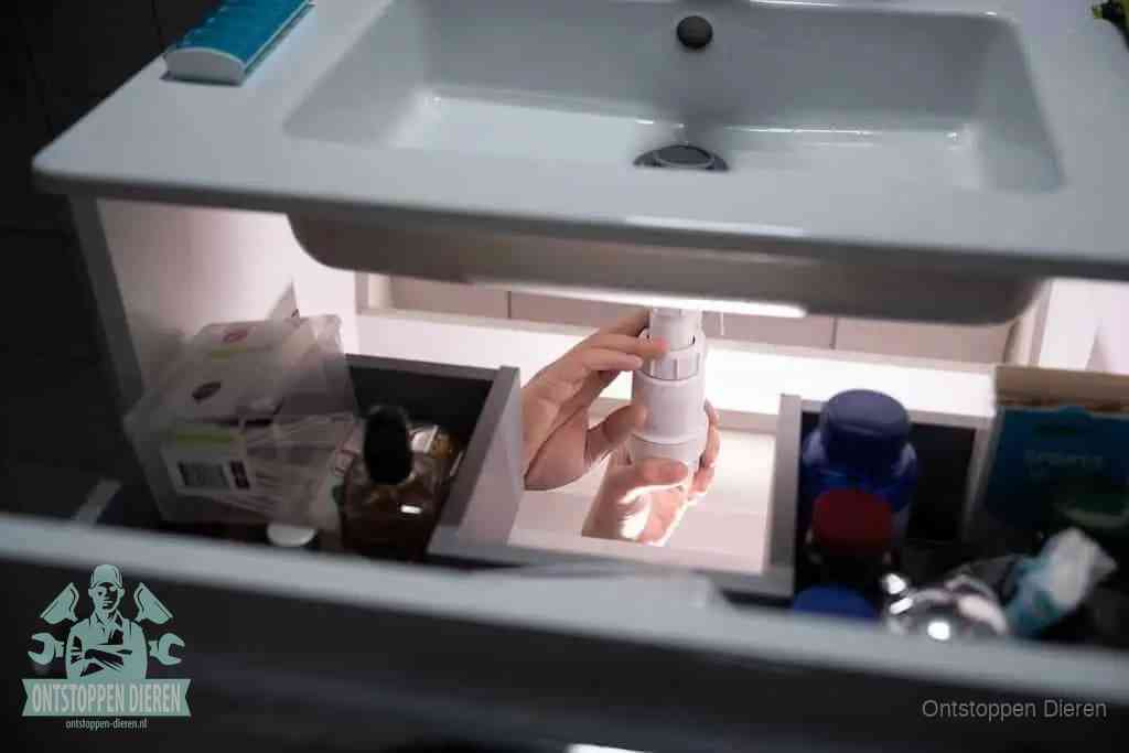 Een pompfles met zeep boven een wastafel in de toiletruimte, de warm water en afwasmiddel-methode om de wc te ontstoppen in Dieren