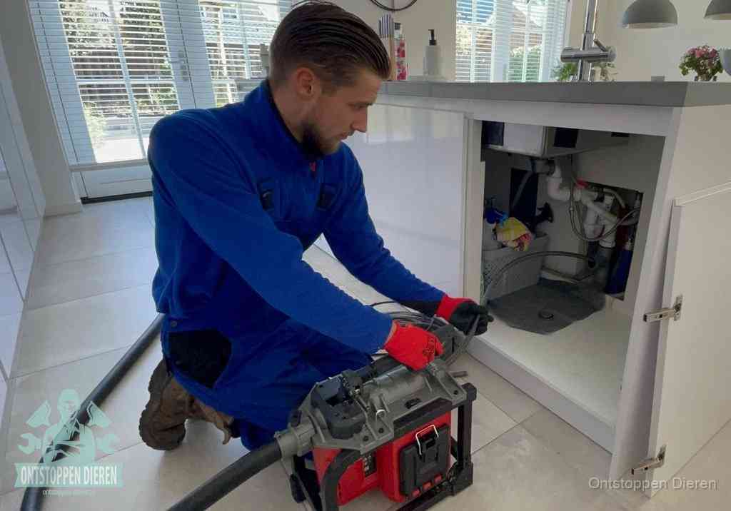 Een monteur voert een professionele elektrische ontstoppingsmachine in de afvoer onder de spoelbak tijdens het gootsteen ontstoppen in Dieren